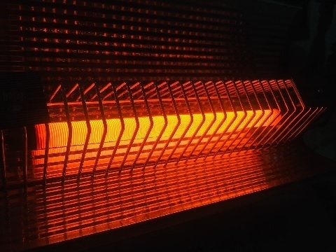 A photo of an old bar radiator heater turned on, the heat elements glowing red in a dark room