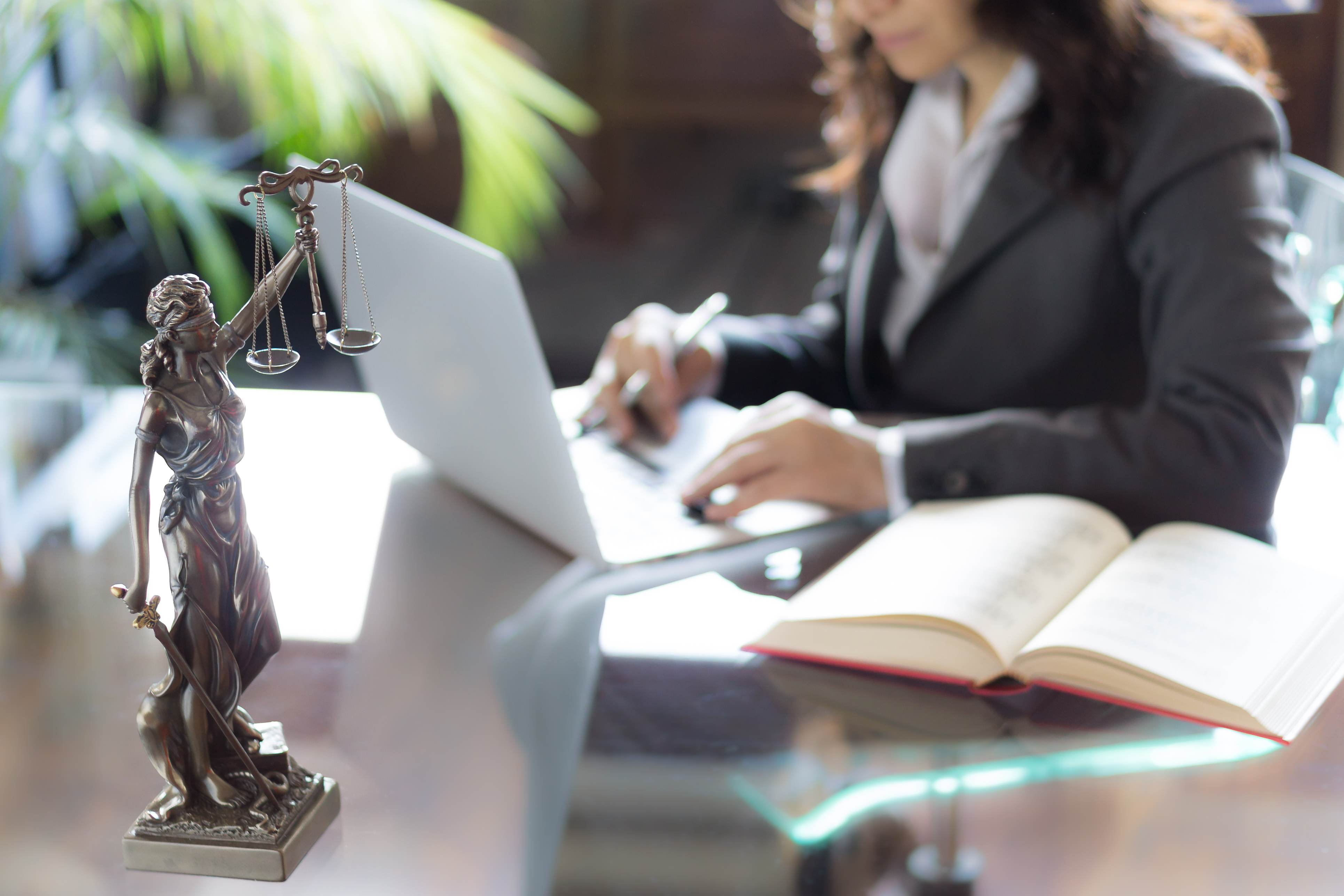 Lawyer office. Statue of Justice with scales and lawyer working on a laptop. Governance concept.