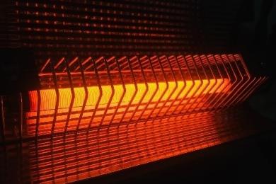 A photo of an old bar radiator heater turned on, the heat elements glowing red in a dark room