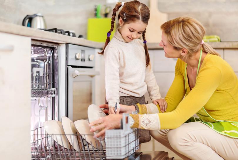 Adult and child in kitchen loading a dishwasher together
