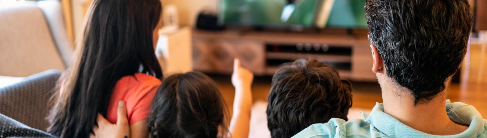 Two adults and children sitting and watching television